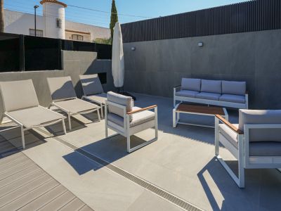 Buitenterras met modern wit-grijs lounge meubilair, gecombineerde porseleinen tegels en composiet vlonder. Ligstoelen en een zithoek zijn zichtbaar.