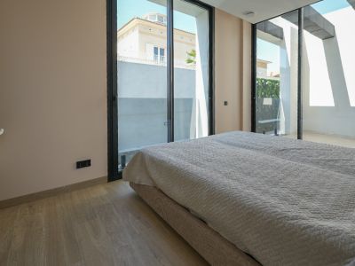 Lichte slaapkamer met lichte houten vloer en grote zwart-omlijste schuifpuien, die uitzicht bieden op een naburig huis en een groene buitenmuur.