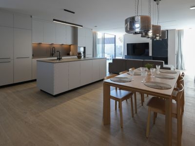 Minimalistische designkeuken met kookeiland en zwarte kraan, open naar een elegante houten eethoek met zes stoelen en moderne hanglampen.
