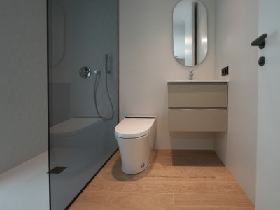 Moderne badkamer met inloopdouche, donker glas en grijs getextureerde wand, zwevend toilet, hangend wastafelmeubel en lichte houtlook vloertegels.