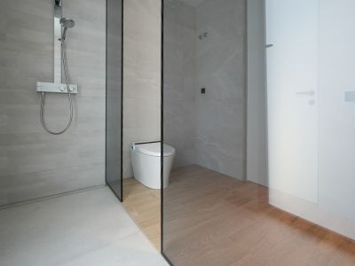 Moderne badkamer met inloopdouche, lichtgrijze tegels en chromen thermostaatkraan. Een glazen wand scheidt de douche van het smart toilet met houtnerf tegels op de vloer.
