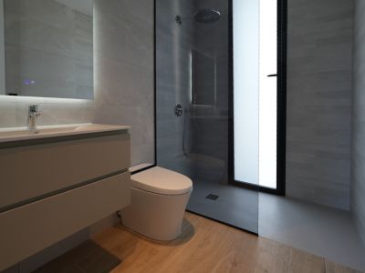 Moderne badkamer met zwevend wastafelmeubel, verlichte spiegel, wandcloset en inloopdouche met regendouchekop, afgewerkt met grijze tegels en een houtlook vloer.