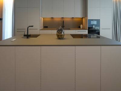 Moderne designkeuken met kookeiland, geïntegreerde spoelbak, inductiekookplaat en neutrale kasten.