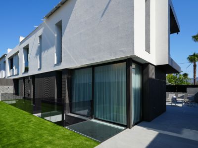 Moderne villa-exterieur met contrasterende wit-grijze en donkere gevels, grote glazen schuifdeuren, kunstgrasgazon en een betegeld terras met buitenmeubilair.