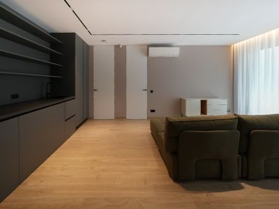 Moderne woonruimte met donkergrijze geïntegreerde kitchenette, lichte houtlook vloer en groene modulaire bank. Vlakke deuren en natuurlijk licht.