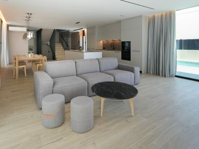 Open woon- en eetruimte met modulaire bank, marmeren salontafel en geïntegreerde keuken, verbonden met het buitenzwembad via grote ramen.