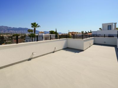 Ruim dakterras met lichte vloertegels en moderne glazen balustrade, met panoramisch uitzicht op bergen en de omliggende stad.