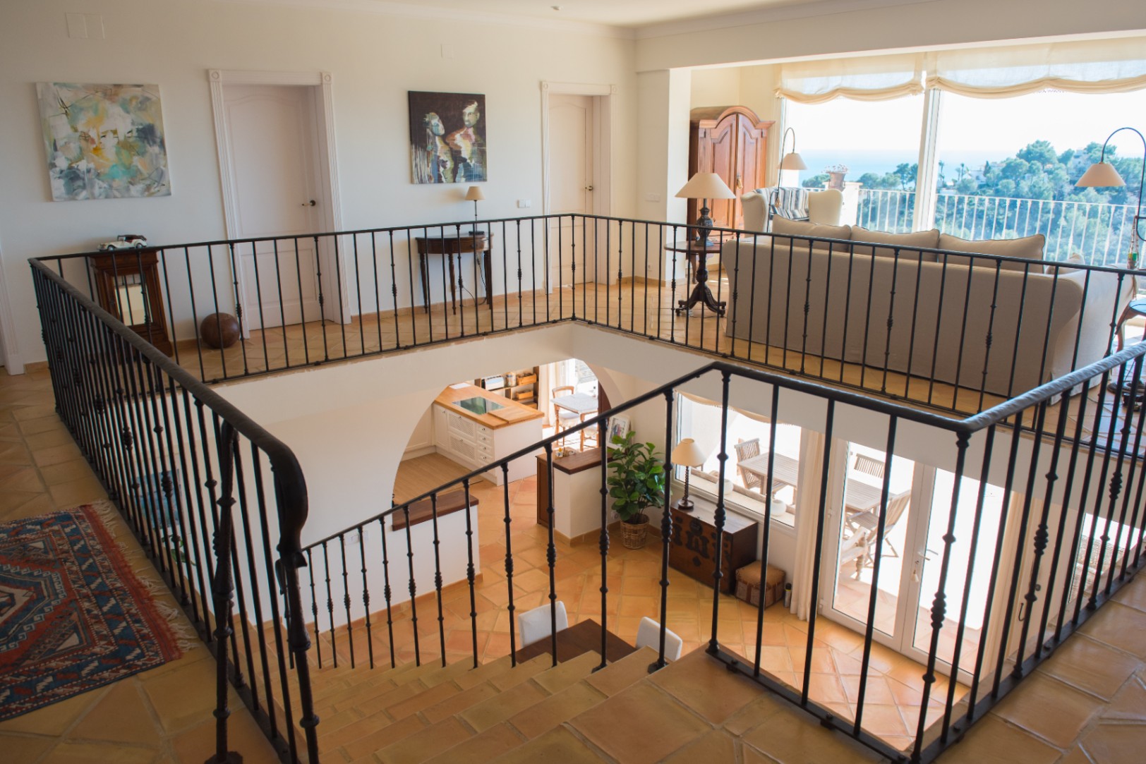 Bovenverdieping met smeedijzeren balustrade en terracotta tegels, met uitzicht op de benedenverdieping en panoramische ramen met zicht op de kust.