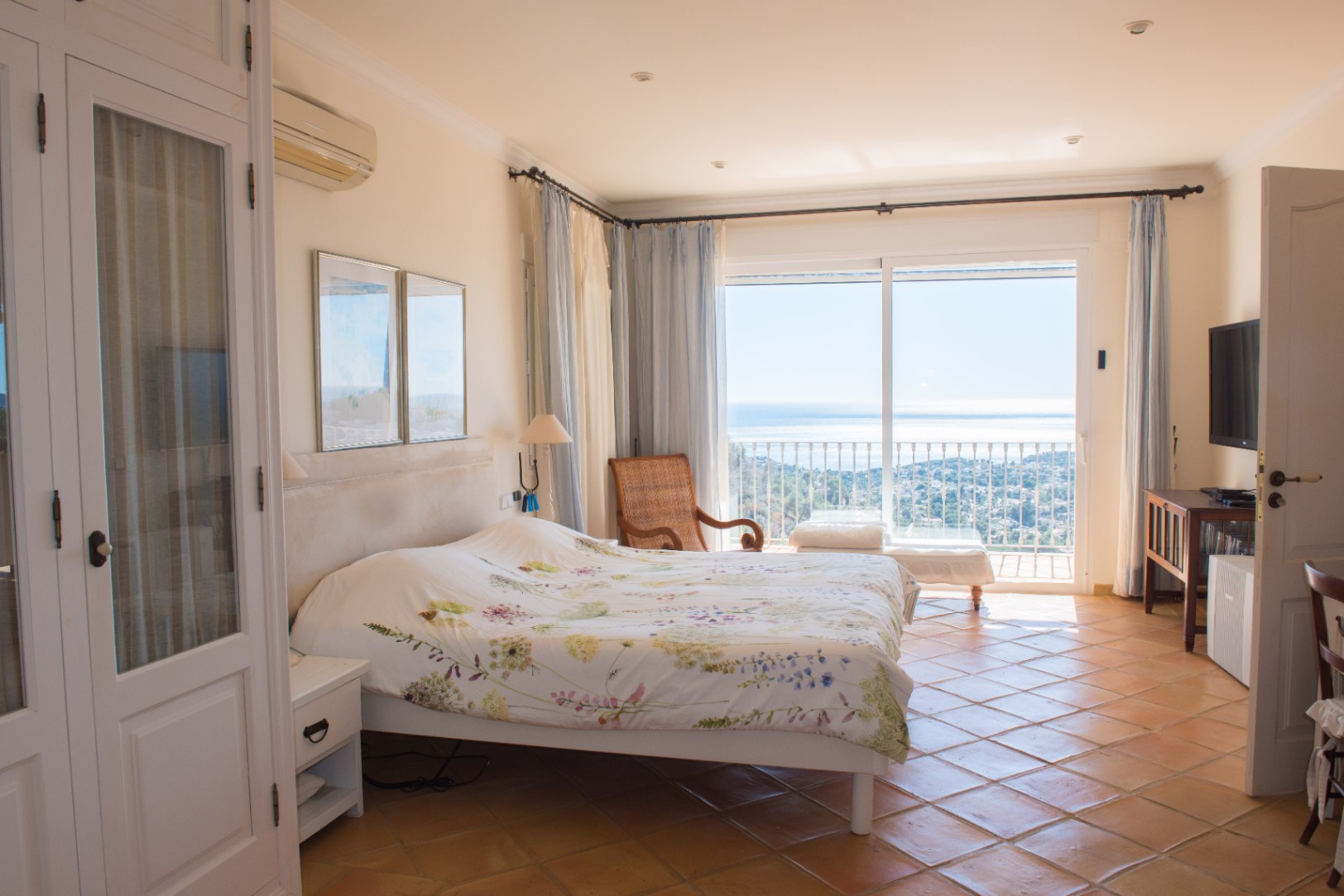 Lichte slaapkamer met terracotta tegelvloer, witte inbouwkasten en een schuifpui naar een balkon met weids uitzicht over de Middellandse Zee.