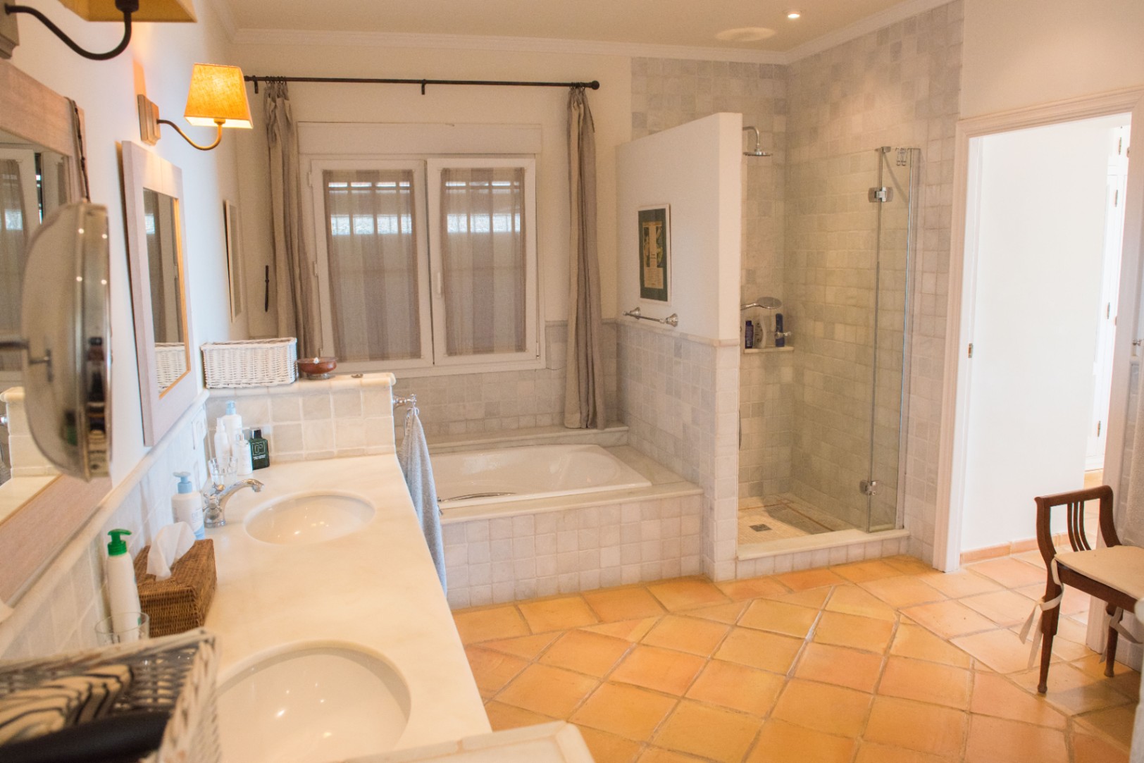 Ruime badkamer met dubbele marmeren wastafel, terracotta vloertegels, een ingebouwd ligbad en een aparte inloopdouche met glazen wand.