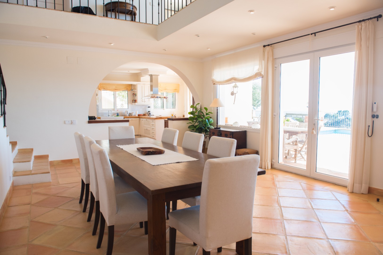 Ruime eetkamer met een massief houten tafel, terracotta tegelvloer en een boogdoorgang naar de keuken, met directe toegang tot het terras en zwembad.