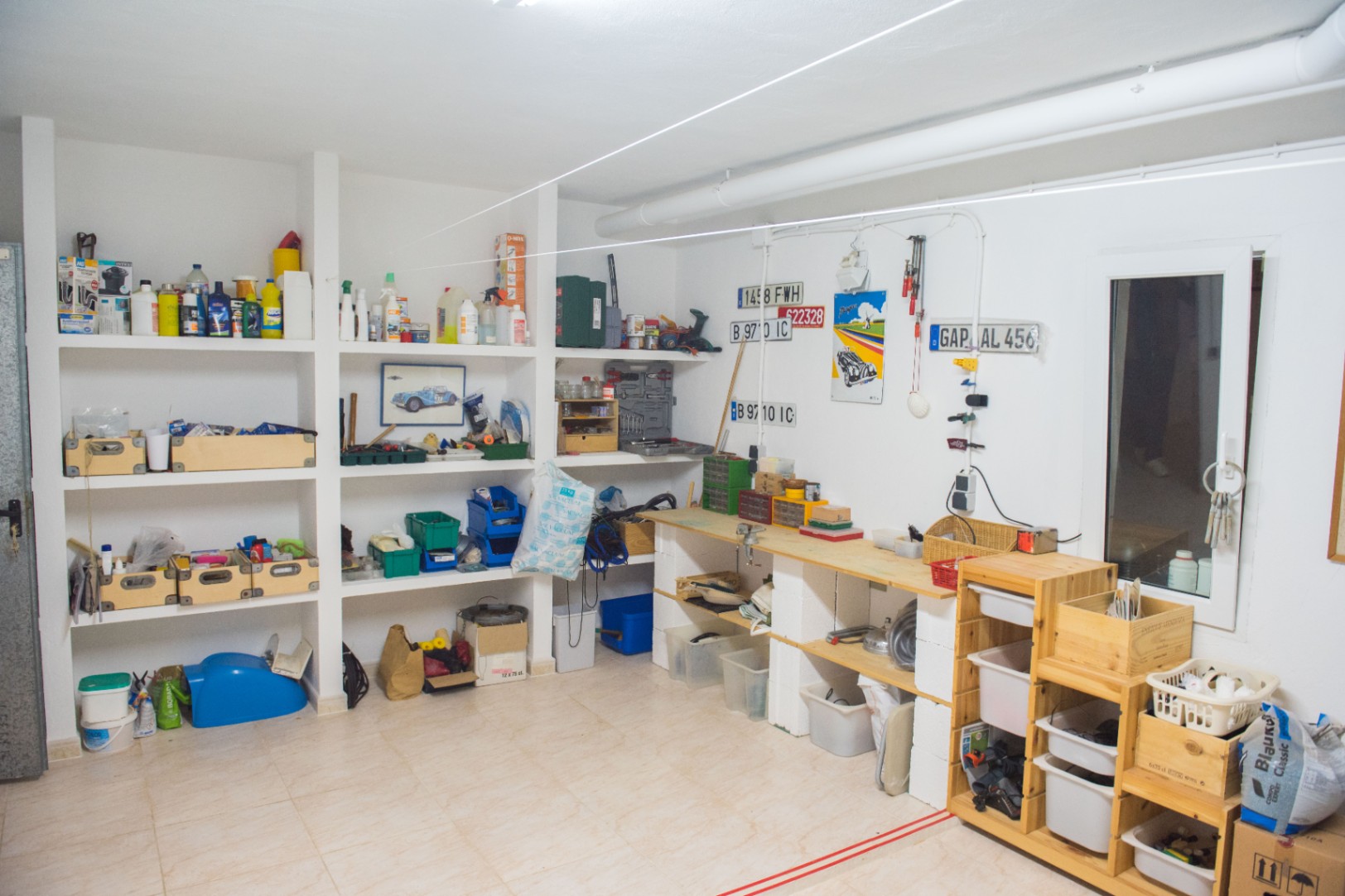 Ruime werkplaats en opslagruimte met ingebouwde gemetselde planken, een houten werkbank en tegelvloer voor onderhoud en hobbyprojecten.