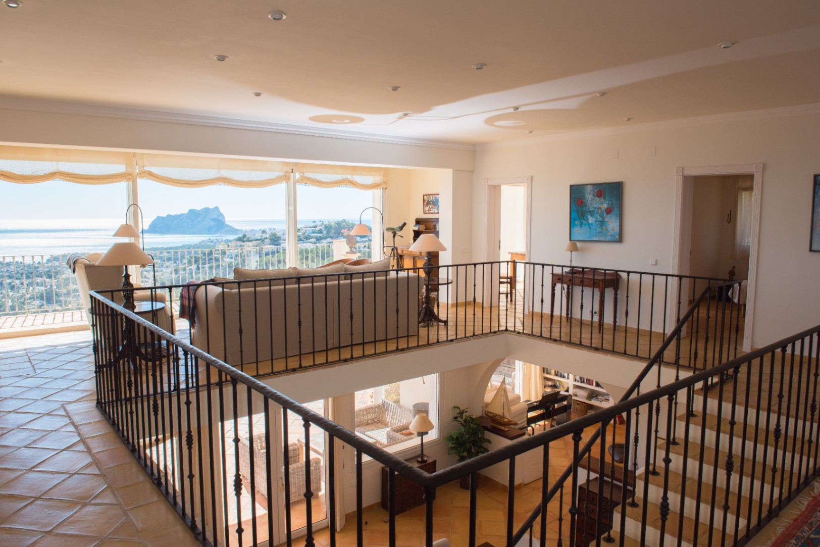 Woonruimte op de bovenverdieping met smeedijzeren balustrade, terracotta vloertegels en grote ramen met panoramisch uitzicht op zee en de Peñón de Ifach.