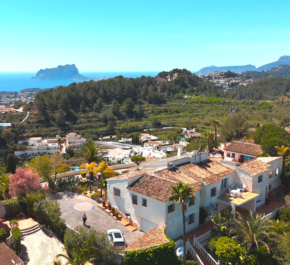 Luchtfoto van de mediterrane villa met terracotta daken, weelderige tuinen en een panoramisch uitzicht op de zee en de Peñón de Ifach.