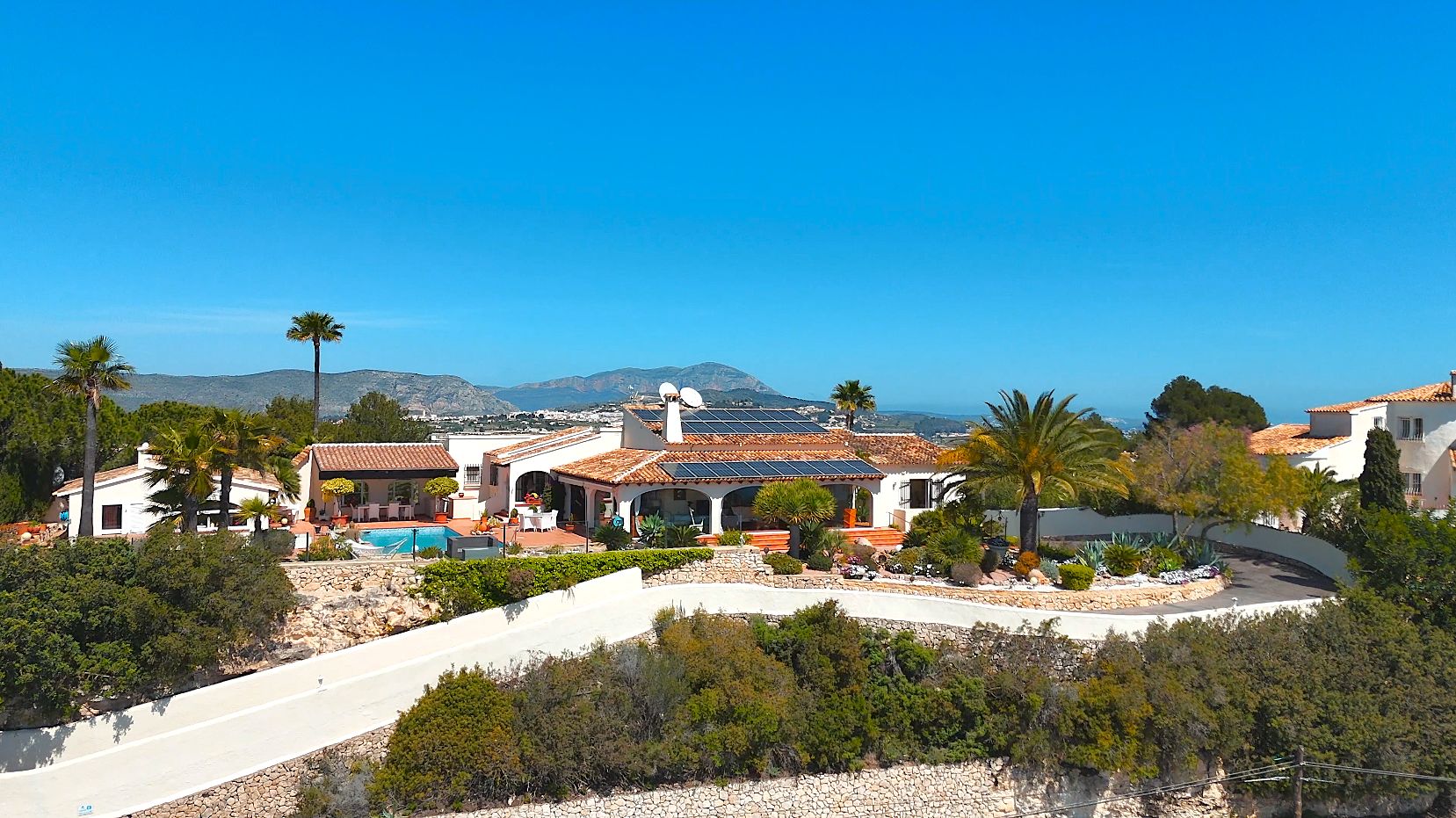 Luchtfoto van de villa met terracotta daken, zonnepanelen en zwembad, omgeven door mediterrane tuinen met panoramisch uitzicht op zee.