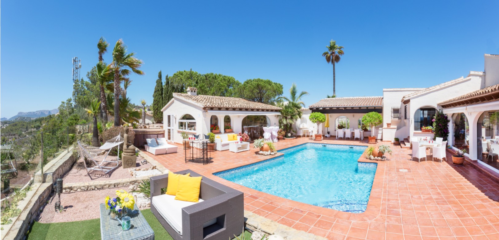 Terras met een rechthoekig zwembad, terracotta tegels en diverse zithoeken. De mediterrane architectuur kenmerkt zich door witte muren en boogvensters.