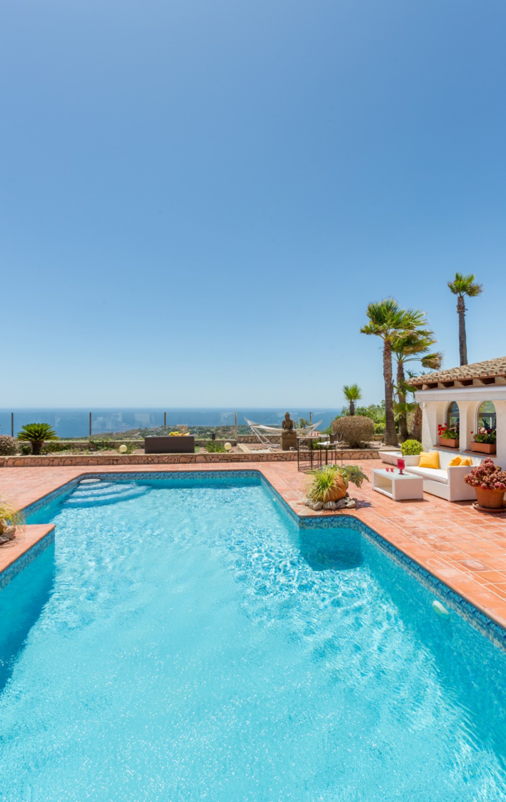 Zwembad met blauwe mozaïektegels en terracotta terras met loungehoek, palmbomen en panoramisch uitzicht op de Middellandse Zee.