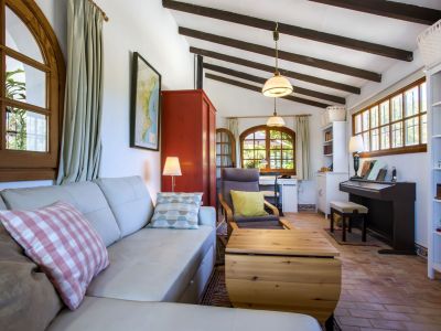 Lichte woonkamer met leren bank, houten balken en terracotta vloeren, die woon- en werkruimtes combineert.