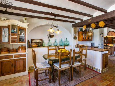 Rustieke eetkamer met ovale tafel, houten stoelen en traditionele kast. Houten balken zichtbaar aan het plafond.
