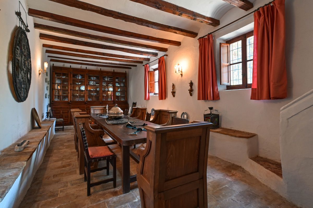 Historische eetkamer met houten balkenplafond, terracotta vloer en een grote ingebouwde houten servieskast met traditioneel keramiek.
