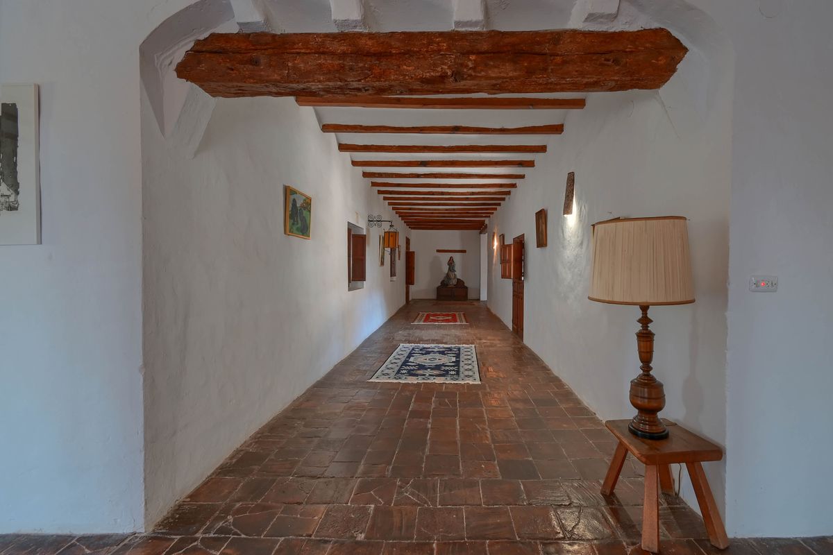 Lange gang met authentieke terracotta vloertegels, witgekalkte muren en een plafond met robuuste, zichtbare houten balken.