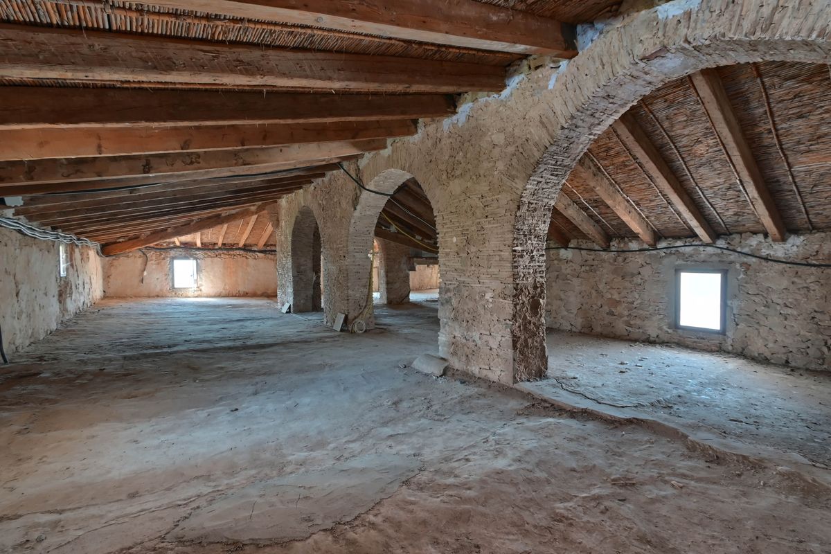 Open zolderruimte met originele houten balken, traditionele rieten plafonds en structurele bogen van natuursteen en baksteen.