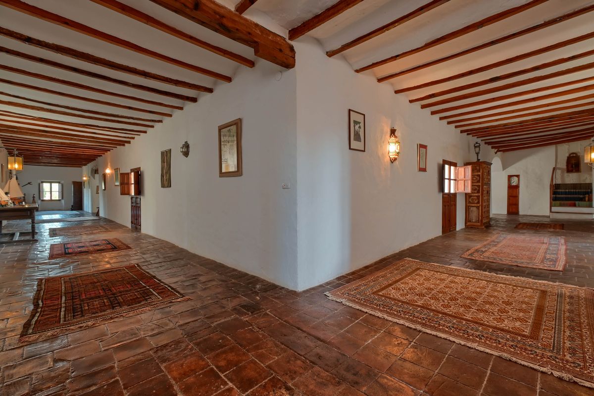 Ruime gang met authentieke houten plafondbalken, originele terracotta vloeren en traditionele tapijten verlicht door sfeervolle wandlampen.