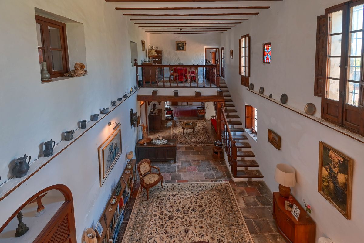 Ruime hal met dubbele hoogte, originele terracotta vloeren, houten balkenplafond en een trap naar een mezzanine met rustieke houten balustrade.