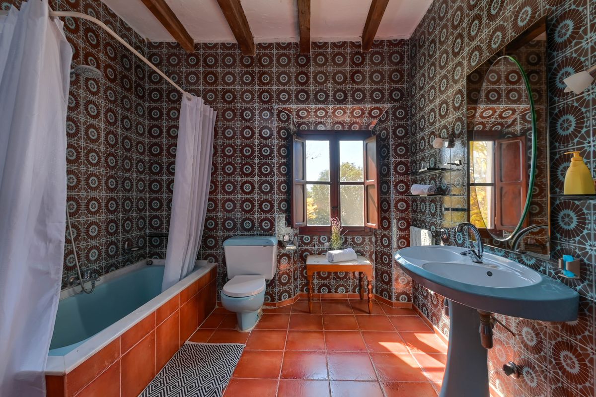 Rustieke badkamer met geometrische wandtegels, pastelblauw sanitair, originele houten balken en een natuurlijke terracotta vloer.
