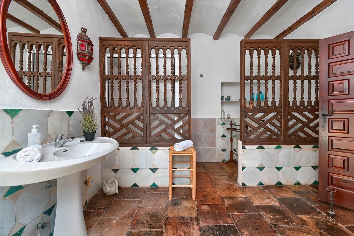 Rustieke badkamer met houten balkenplafond, terracotta vloertegels, een kolomwastafel en traditioneel gesneden houten schermen.