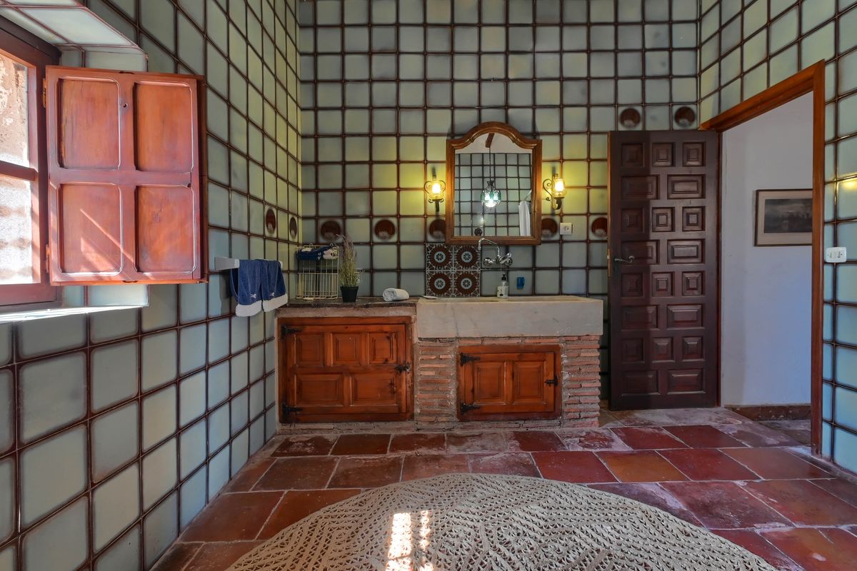 Traditionele badkamer met een stenen wastafel op een bakstenen voet, rustieke houten kasten, terracotta vloertegels en wanden met een ruitpatroon.