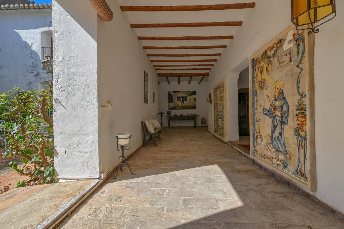 Traditionele overdekte veranda met houten balkenplafond, natuurstenen vloer en een groot historisch religieus tegeltableau aan de zijmuur.