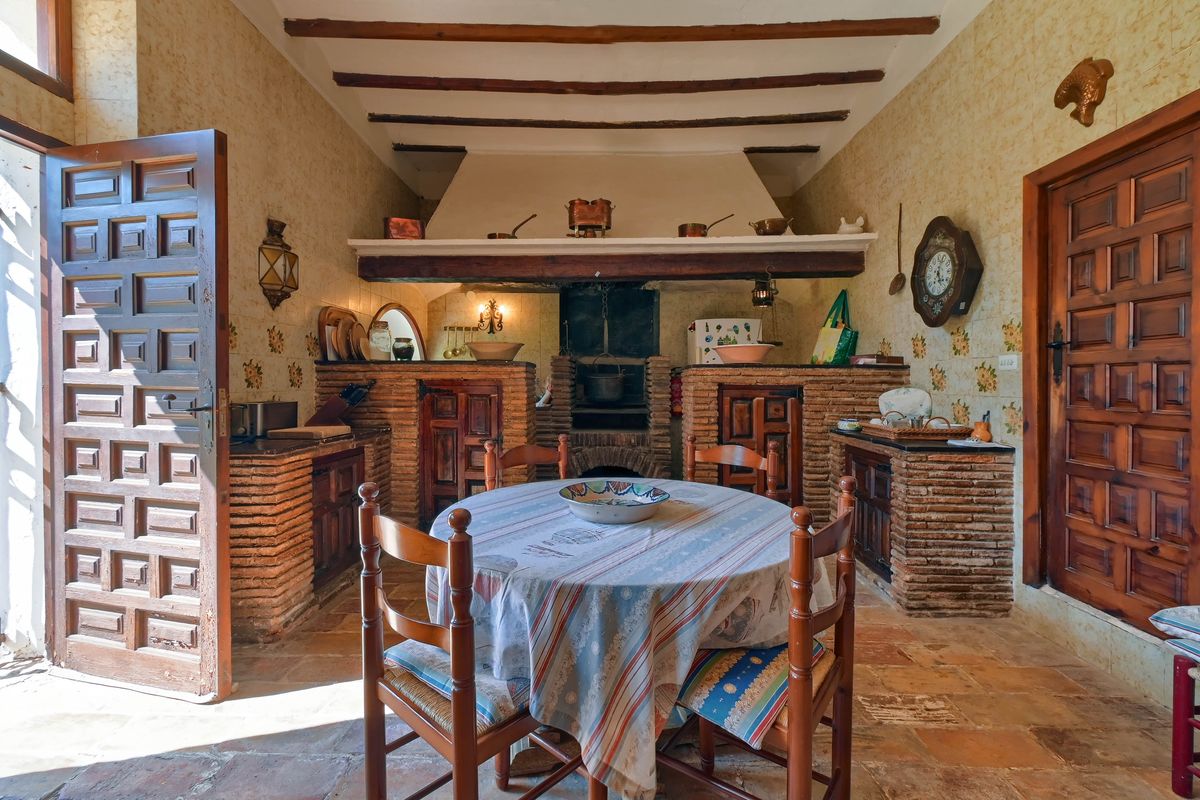 Traditionele rustieke keuken met een grote open bakstenen haard, houten plafondbalken en authentieke terracotta vloertegels.