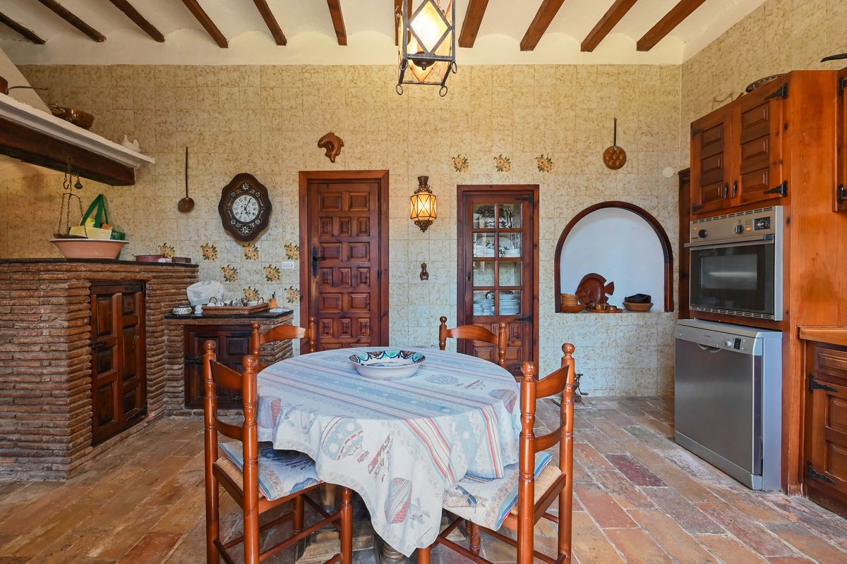 Traditionele rustieke keuken met houten balkenplafond, terracotta vloer en gemetselde haard. Voorzien van gedecoreerde wandtegels en inbouwapparatuur.