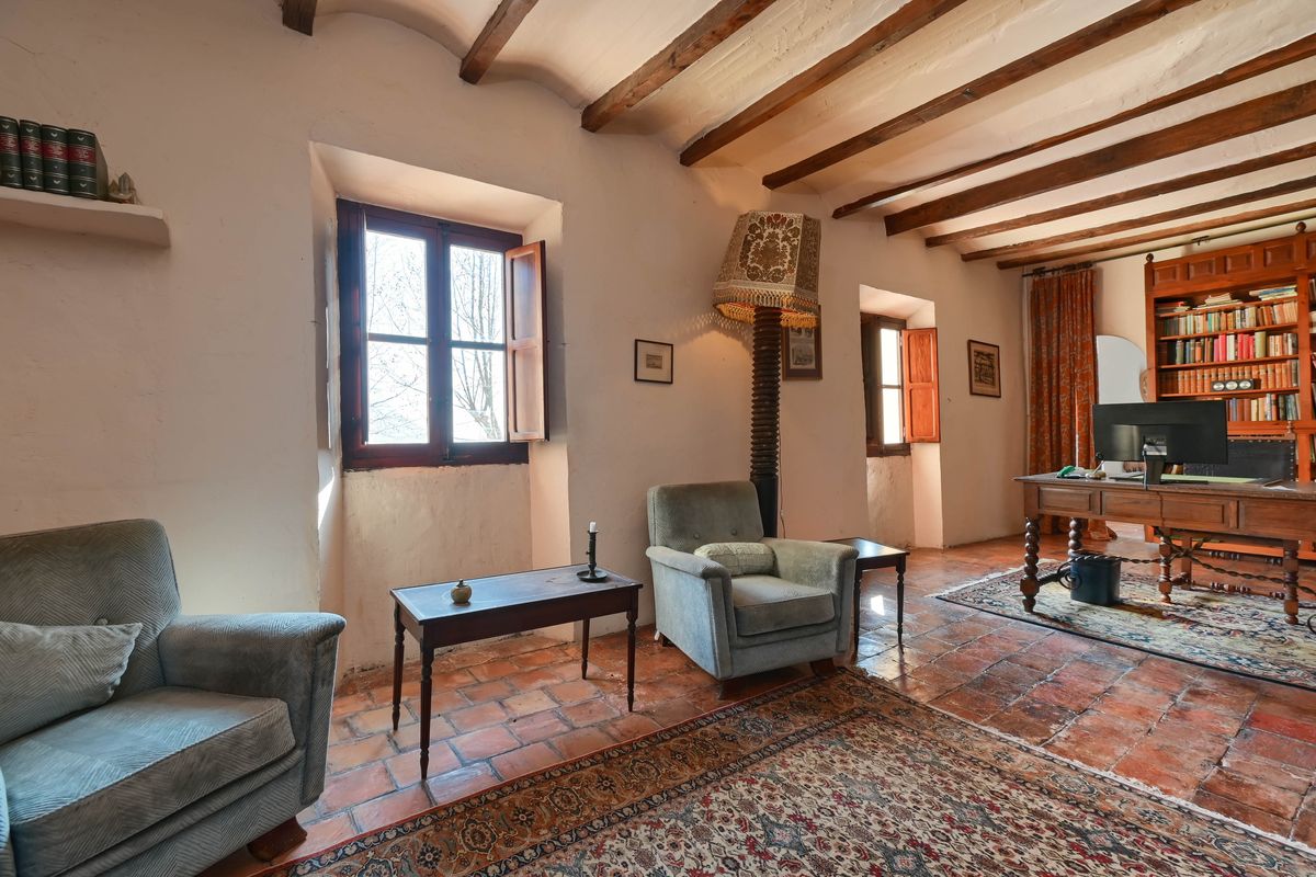 Werkkamer met authentieke houten plafondbalken, terracotta vloeren en diepe vensterbanken. Voorzien van een antiek bureau en ingebouwde boekenkasten.