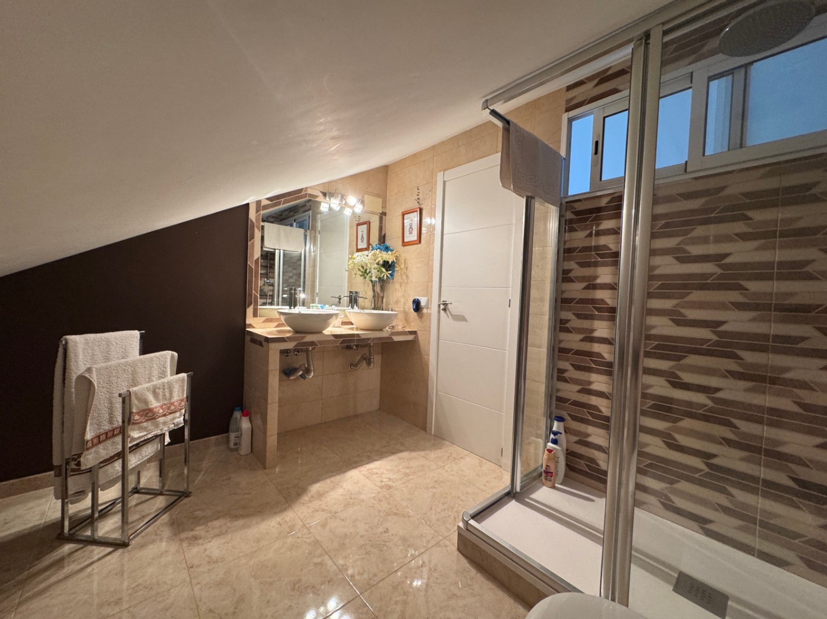 Badkamer met dubbele wastafel en douche met glazen schuifdeuren.