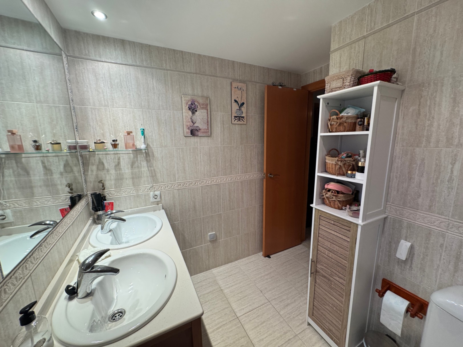 Badkamer met dubbele wastafel, spiegel en opbergrek.
