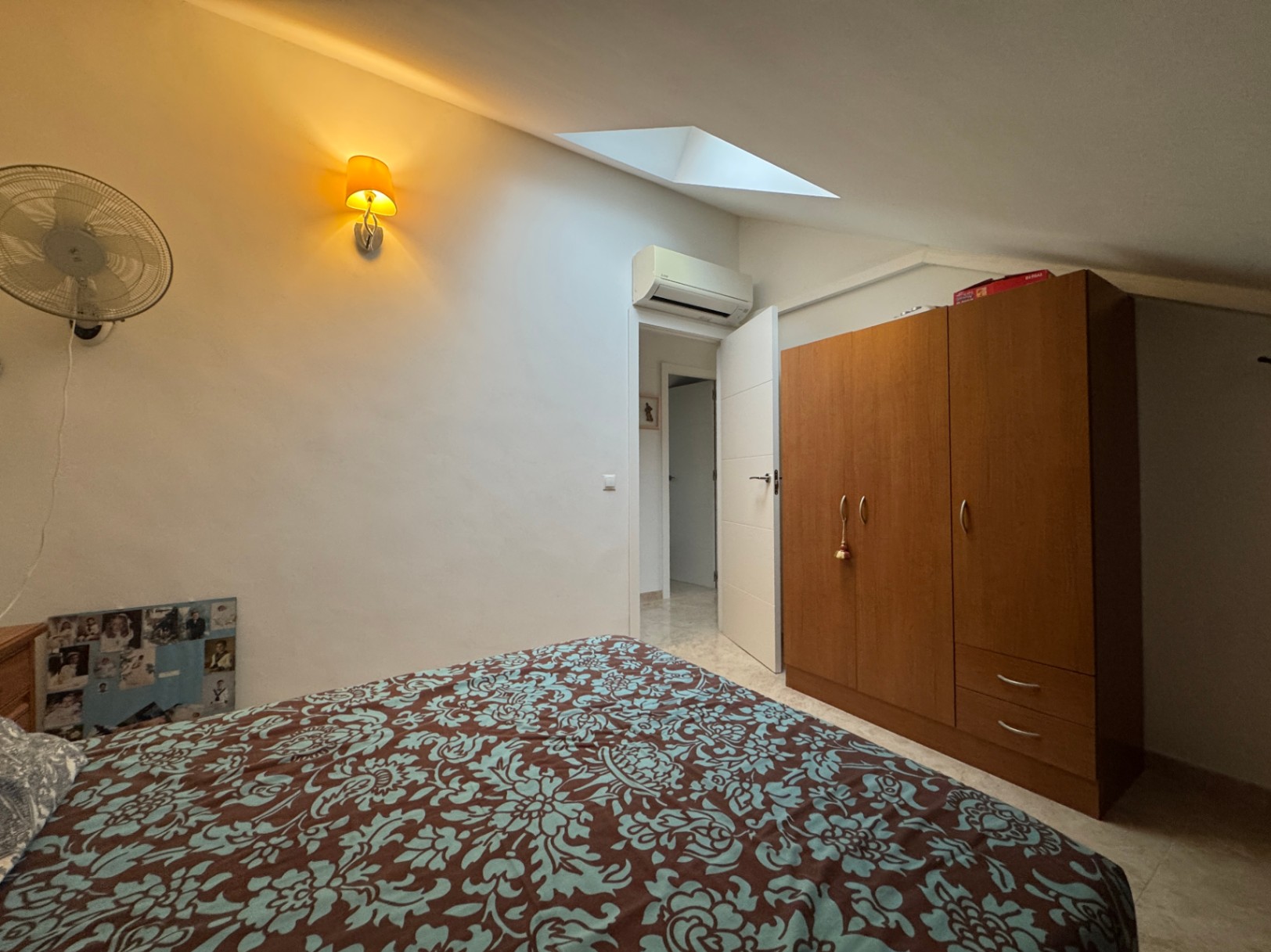 Slaapkamer met een bedsprei met motief, houten kledingkast en warme sfeerverlichting.