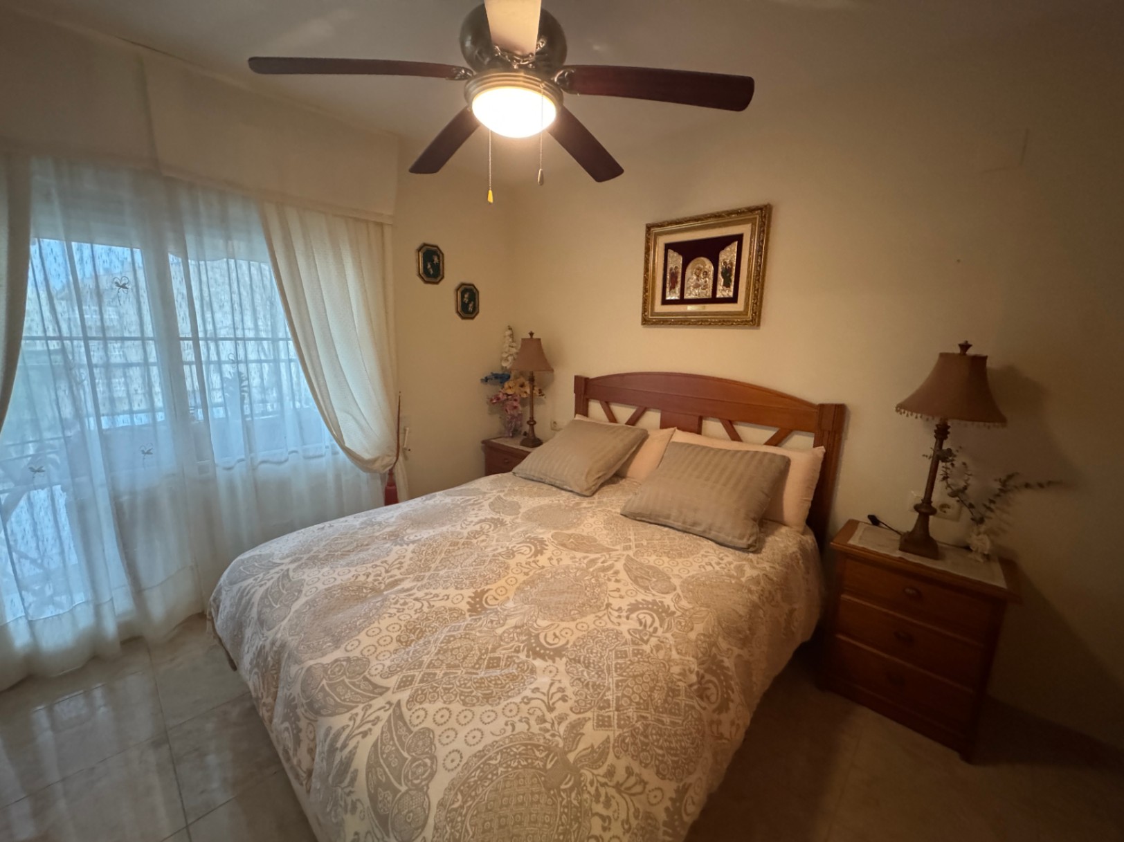 Slaapkamer met houten bed, beddengoed met patroon en plafondventilator met geïntegreerd licht.