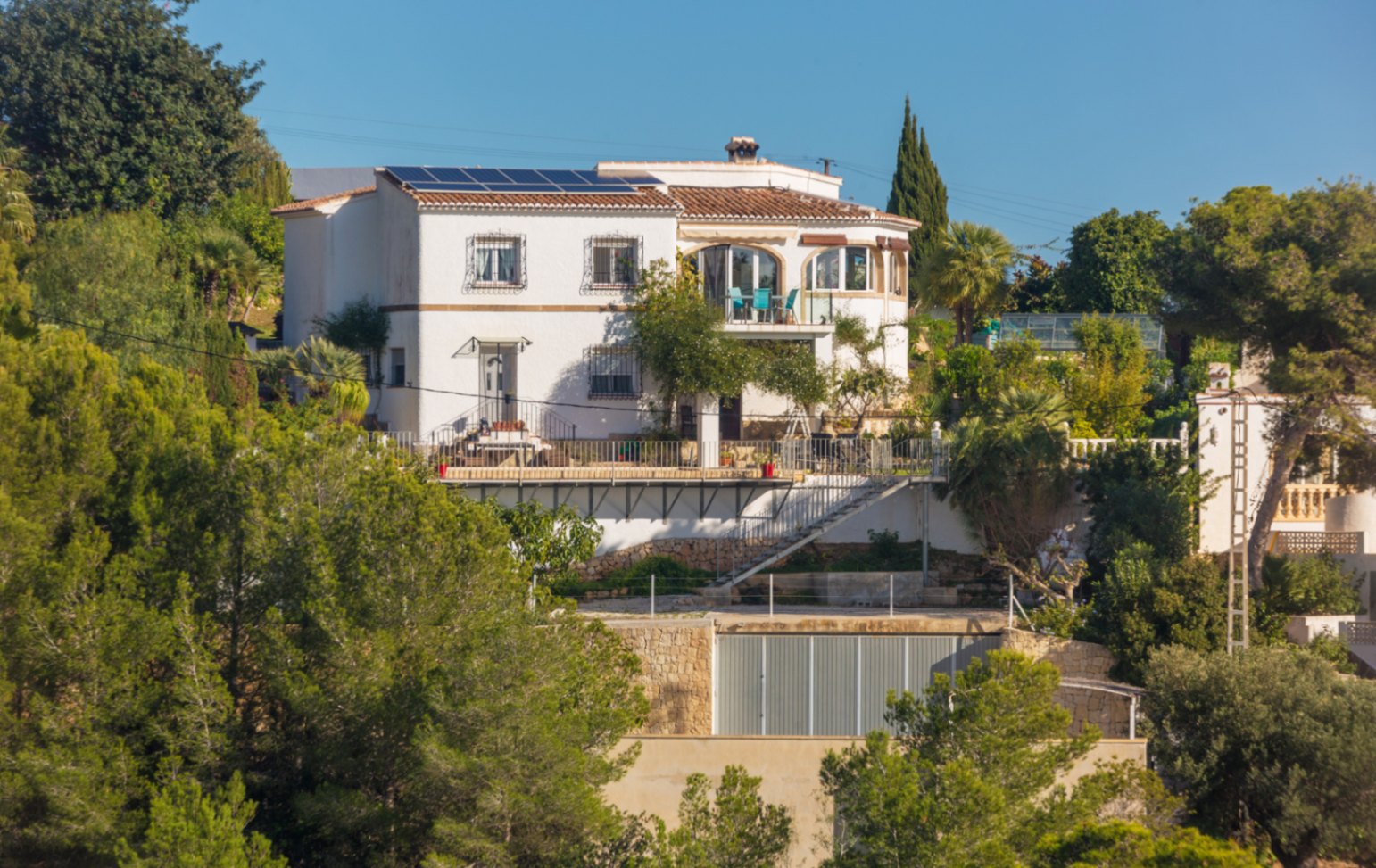 Middellandse Zee-stijl villa met witte gevels, zonnepanelen en diverse terrassen, gelegen op een beboste helling met authentieke natuurstenen muren.