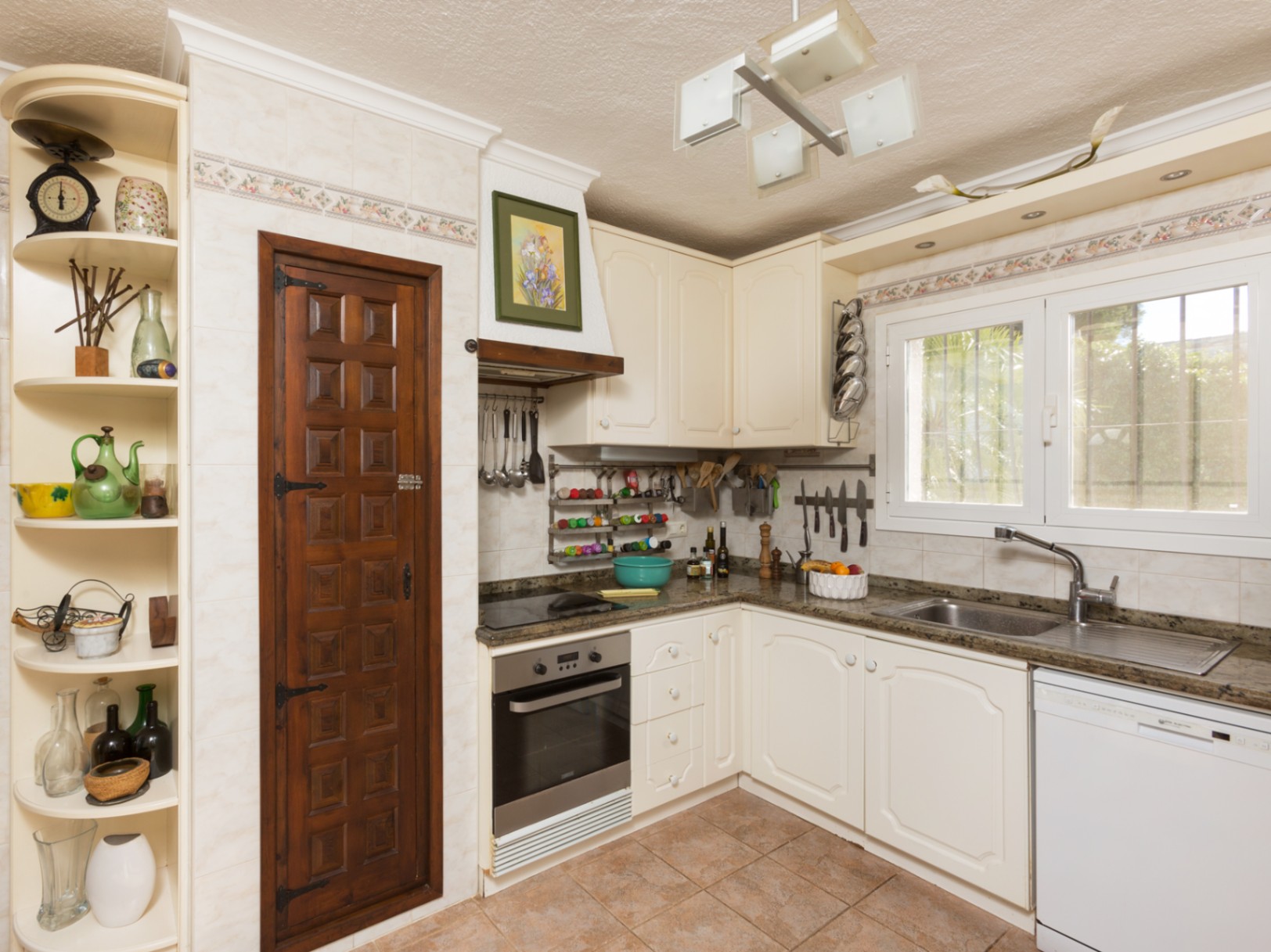 Traditionele keuken met crèmekleurige kasten, granieten werkbladen en een decoratieve donkerhouten voorraadkastdeur. Voorzien van inbouwapparatuur en een tegelvloer.