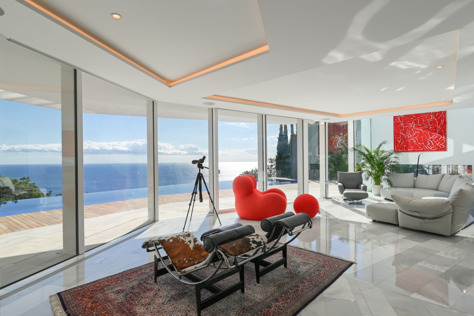 Lichte woonkamer met glazen pui van vloer tot plafond, marmeren vloer en designmeubels met panoramisch uitzicht op de infinity pool en de zee.