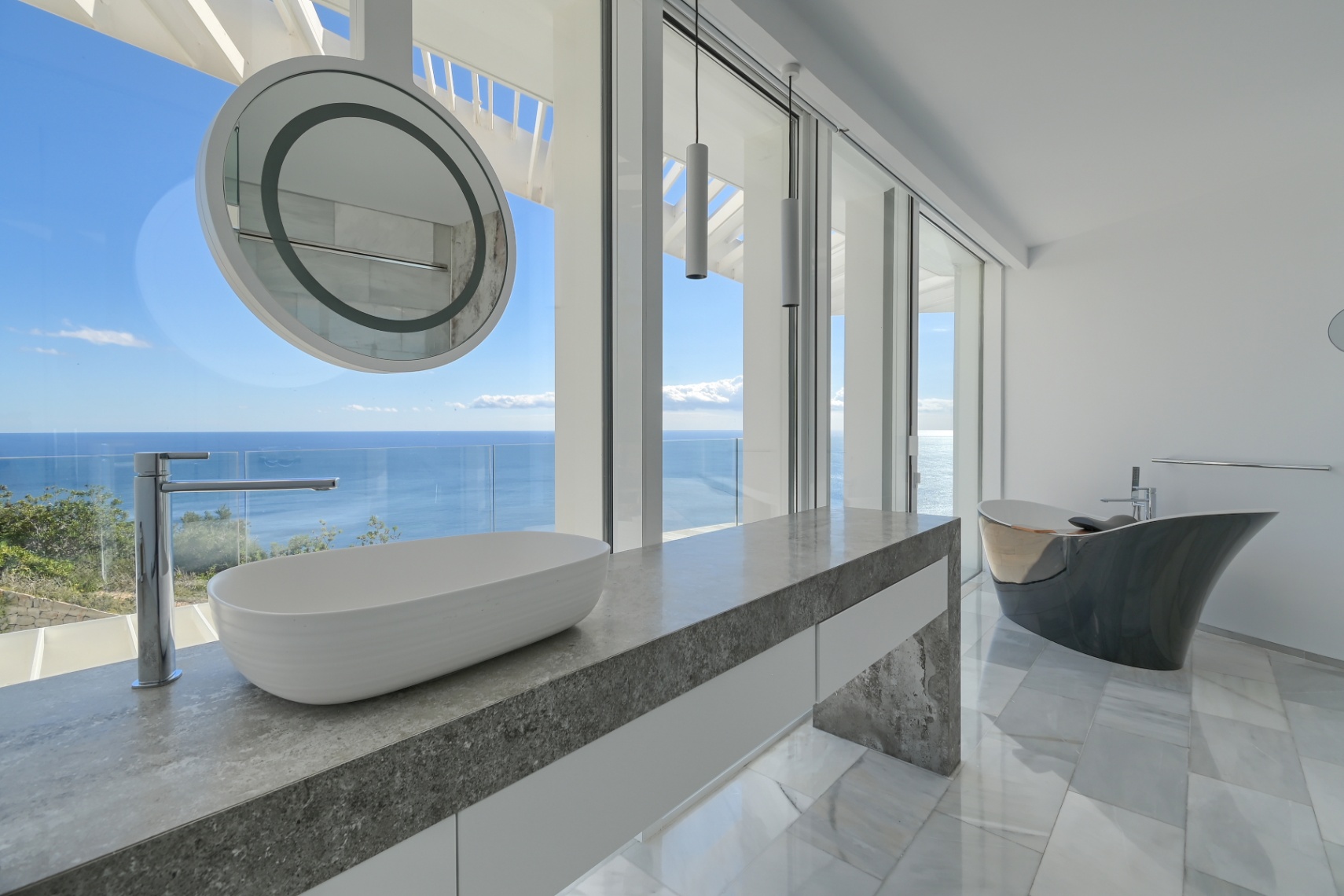 Moderne badkamer met grijs natuurstenen wastafelblad, opbouwkom en een vrijstaand designbad, voorzien van kamerhoge ramen met panoramisch zeezicht.