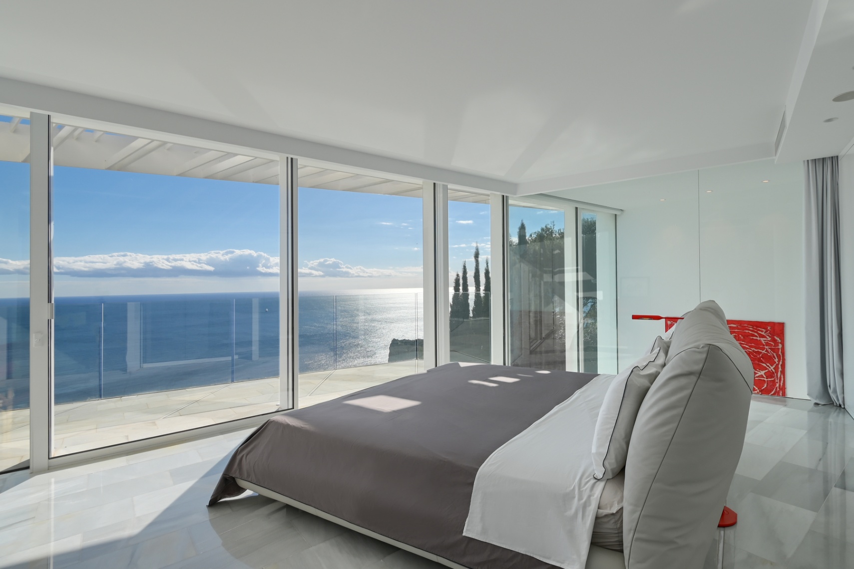 Moderne hoofdslaapkamer met kamerhoge glazen wanden, witte marmeren vloer en panoramisch uitzicht op de Middellandse Zee vanaf een privéterras.