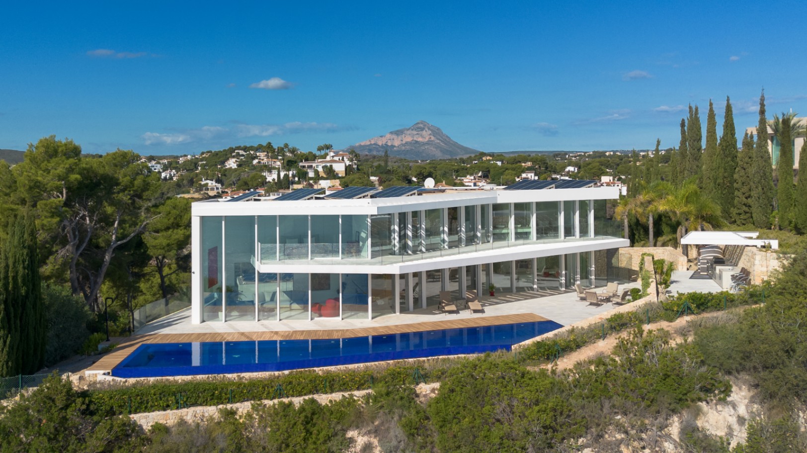 Moderne villa met twee verdiepingen, glazen gevels, een overloopzwembad, zonnepanelen en panoramisch uitzicht op de Montgó-berg.
