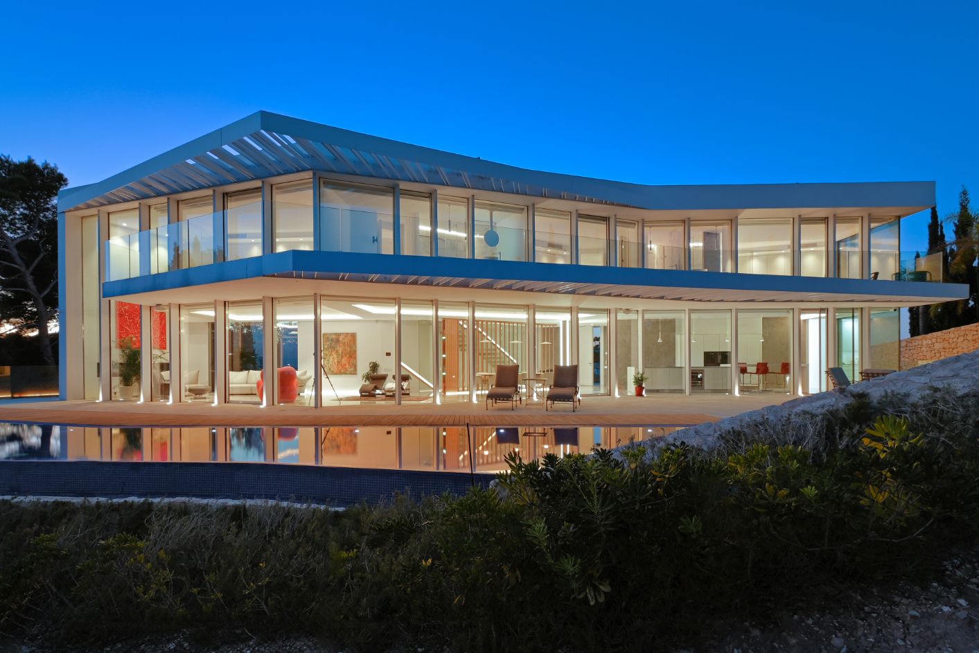 Moderne villa met twee verdiepingen, glazen gevels van vloer tot plafond, een ruim terras met zwembad en geïntegreerde binnenverlichting.