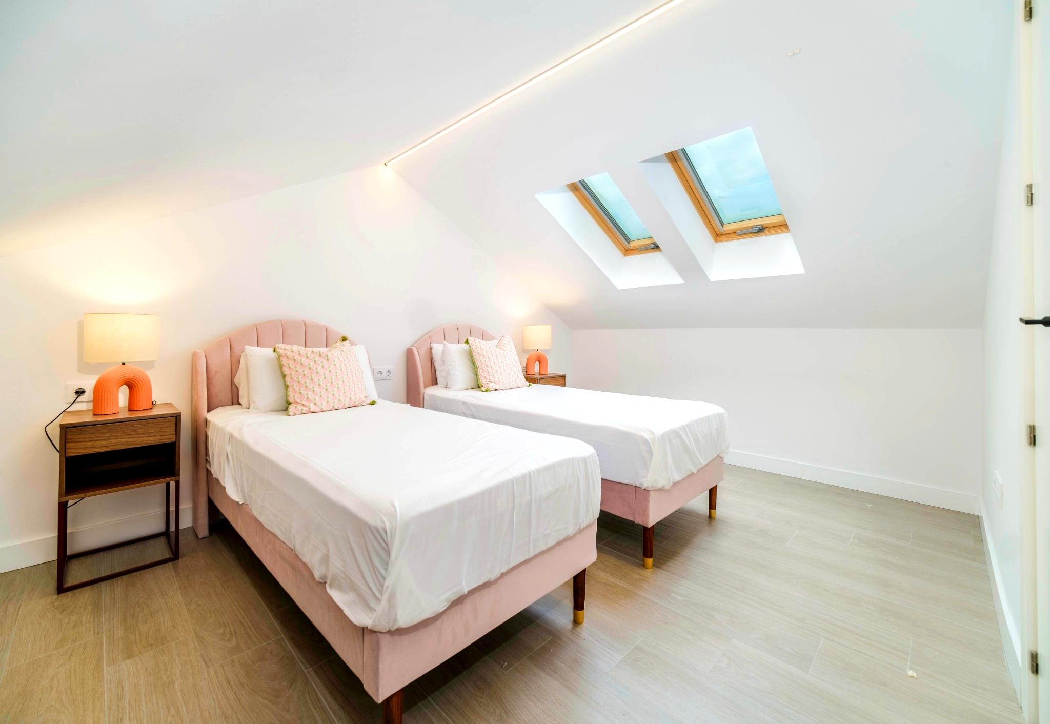 Slaapkamer op de bovenverdieping met twee roze fluwelen eenpersoonsbedden, dubbele dakramen en geïntegreerde LED-verlichting in het schuine plafond.