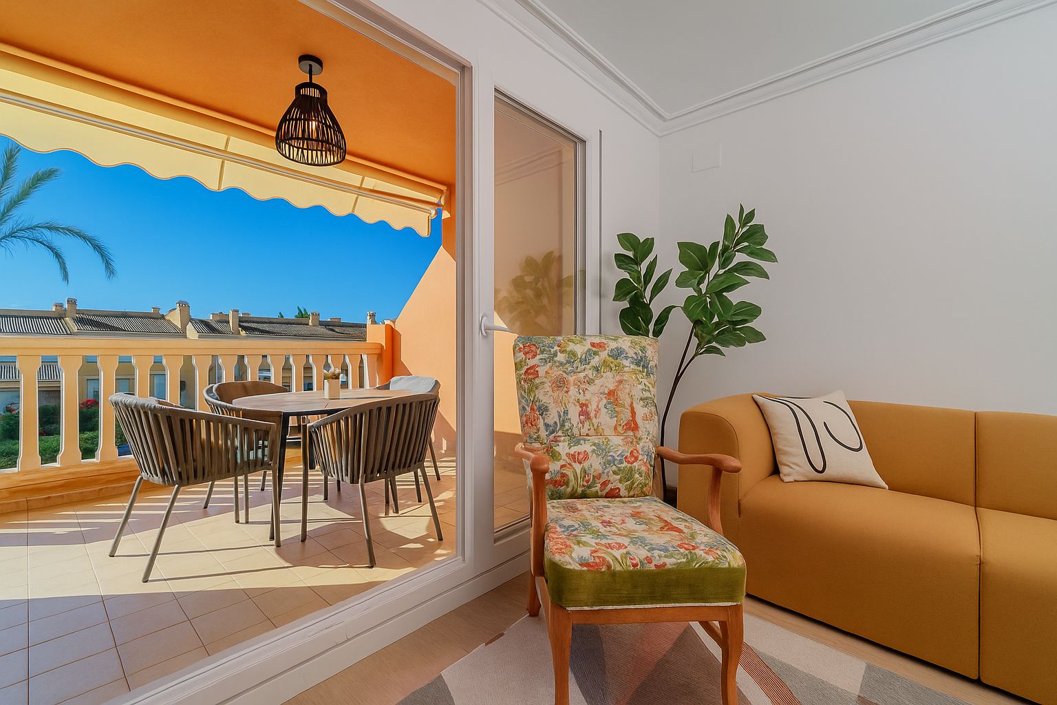 Woonkamer met okergele bank en bloemenfauteuil die uitkomt op een privéterras met eethoek buiten, geel zonnescherm en vrij uitzicht.