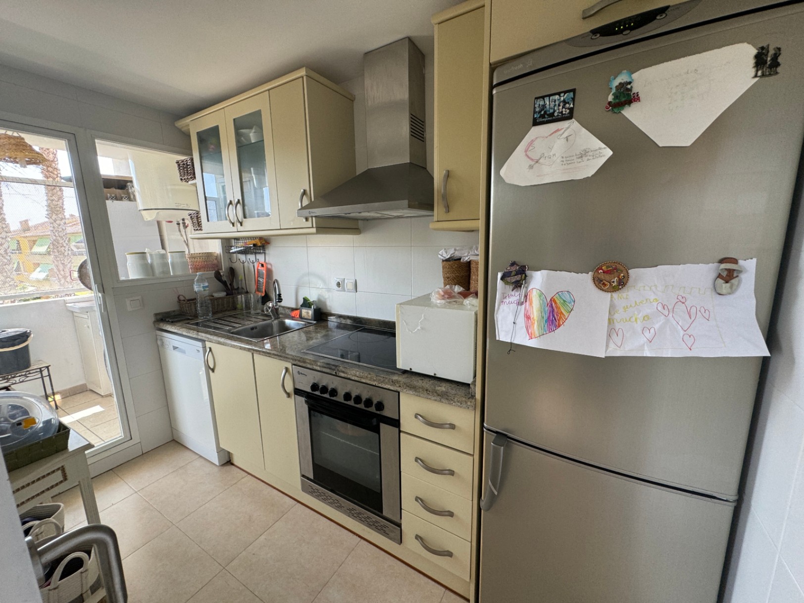 Functionele keuken met crèmekleurige kasten, granieten werkblad en roestvrijstalen apparatuur. Voorzien van inbouwoven, afzuigkap en directe toegang tot het terras.
