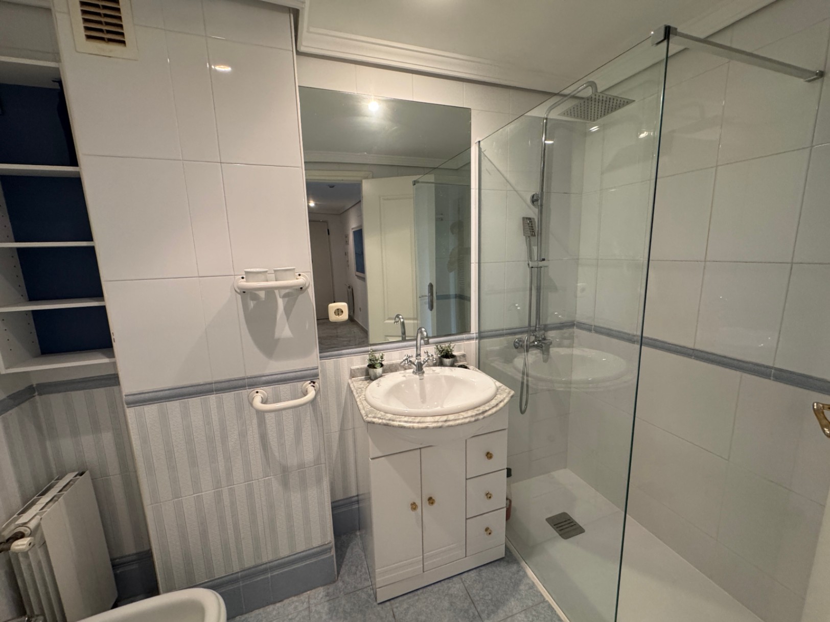 Badkamer met inloopdouche met glazen wand, wit wastafelmeubel met marmeren blad en ingebouwde schappen. Afgewerkt met witte en gestreepte wandtegels.